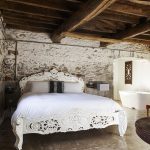 Polished concrete floors and rustic beams create a contemporary bedroom at Devon Farmhouse, to hire at The Big House Company