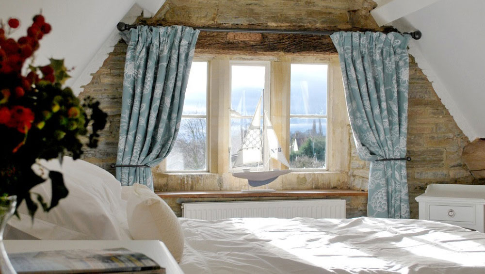 A light filled bedroom with a feature wall of exposed, mellow Cotswold stone.