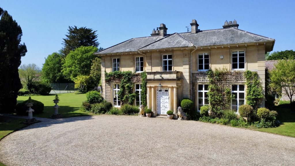 Luxury big house in the English countryside at sunset, golden light over gardens.