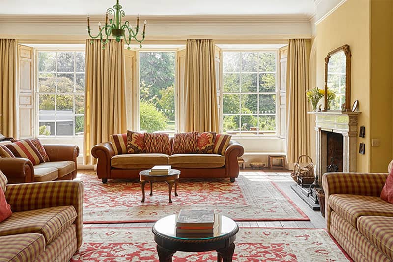 Elegant sitting room at Tone Dale House with large sash windows, traditional sofas, chandelier and fireplace.