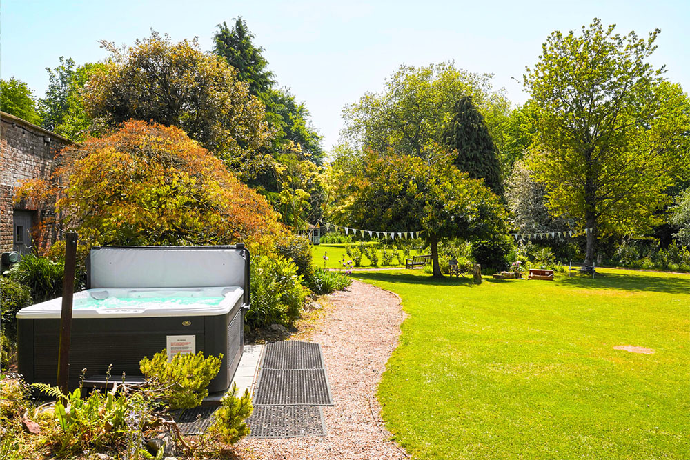Outdoor hot tub set in the gardens of Tysoe Manor, surrounded by green lawn, trees and summer foliage.