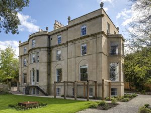 Front exterior of Bath Villa, a large restored Georgian townhouse with tall sash windows, stone façade and landscaped lawn.