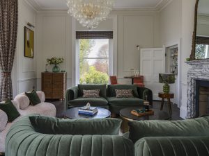 Elegant drawing room at Bath Villa with green velvet sofas, chandelier and tall sash window.