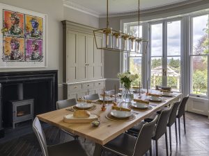 Bright dining room at Bath Villa with long wooden table, upholstered chairs and floor-to-ceiling windows.