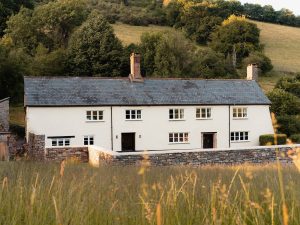 Charming Bampton Longhouse in Devon surrounded by golden fields and rolling hills.