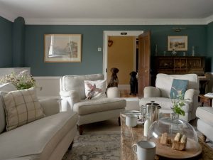 Elegant living room at Bampton Longhouse in Devon with classic furniture, a piano, and two dogs by the doorway — ideal for relaxing group stays and pet-friendly holidays.