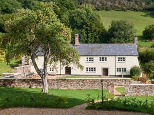 Front view of Bampton Longhouse in Devon surrounded by landscaped gardens and countryside scenery