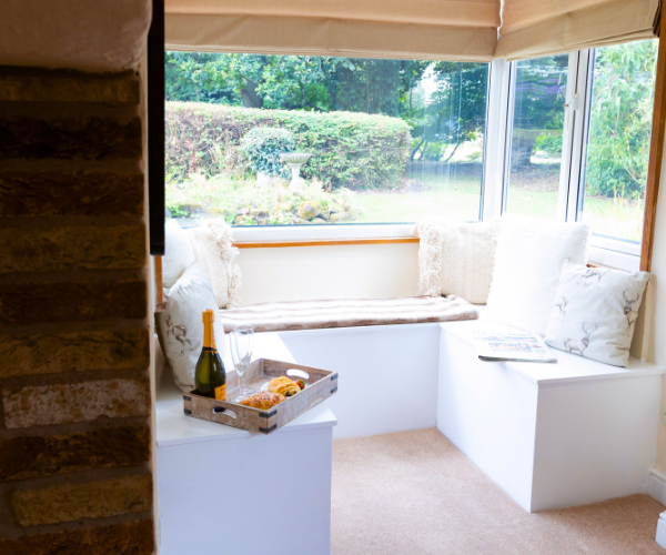 Big Family Gatherings and Party Houses A corner seat looking onto a garden, with cushions and a tray with snacks and a bottle of champagne.