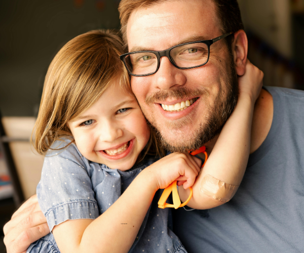 Planning a big family reunion 1 Father with facial hair and glasses and a young girl, holding orange sunglasses with her hands round his neck smiling together during a multi-generational family reunion